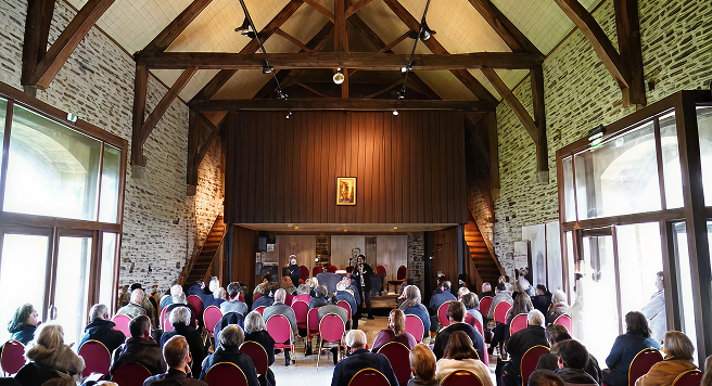 Conférence dans salle en pierre avec public.