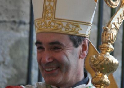 Personne en tenue religieuse, souriant avec une crosse dorée.