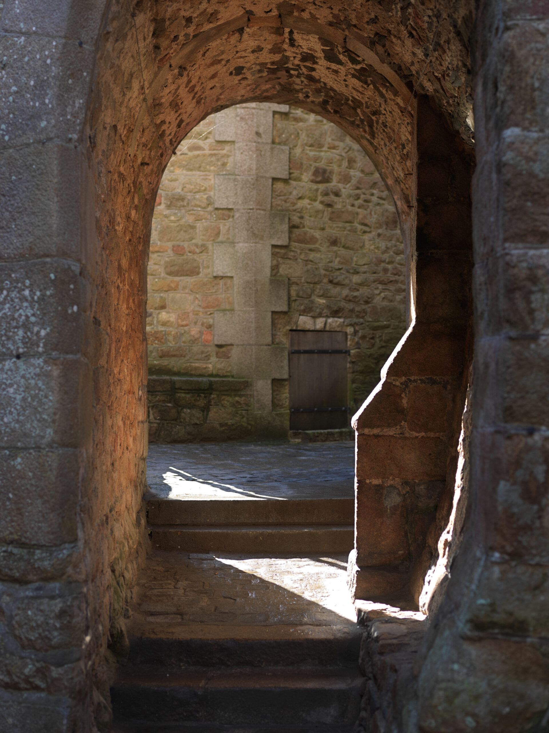 Passage voûté en pierre, lumière sur marches.