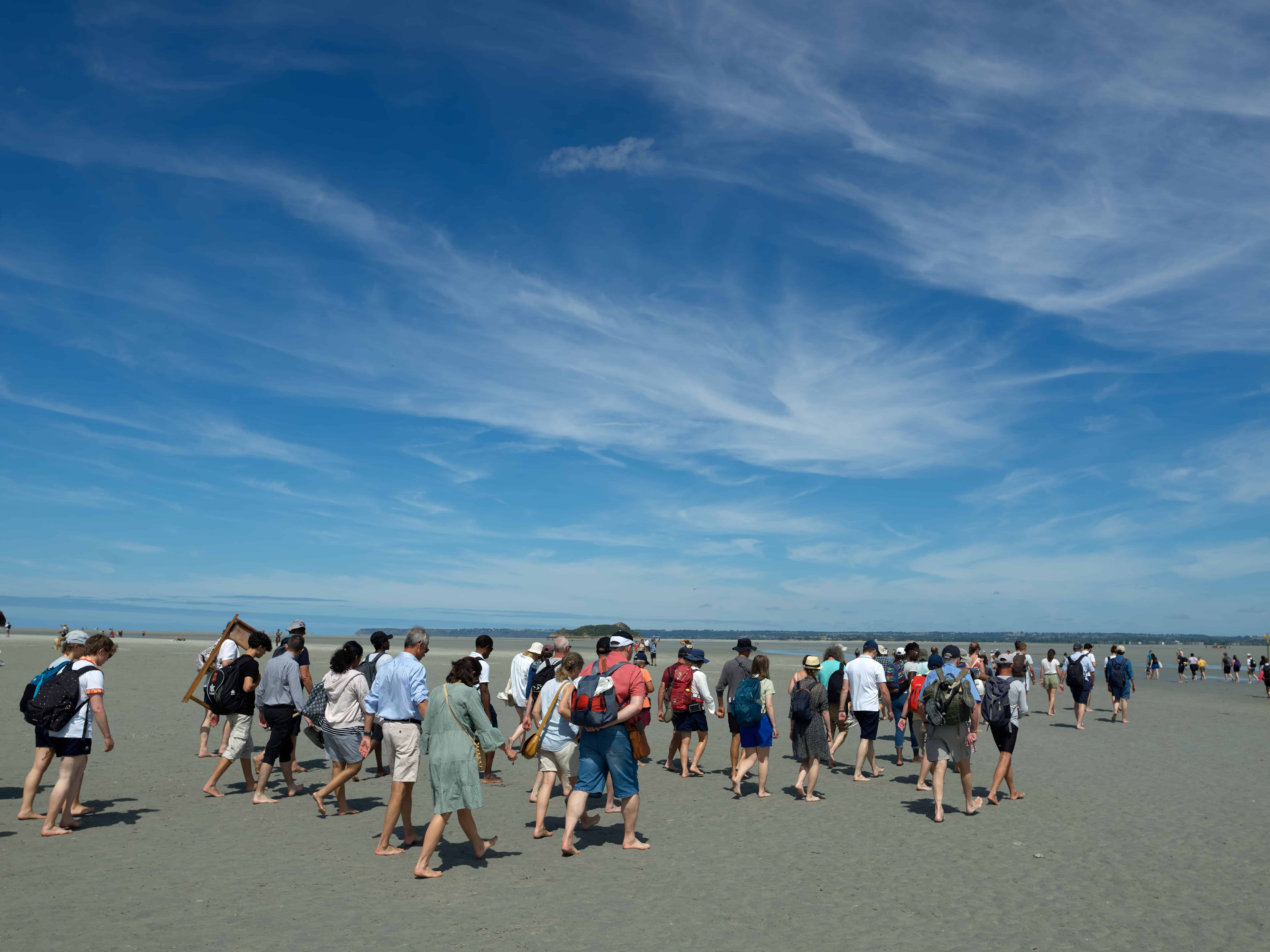 Groupe de personnes marchant sur la plage sous ciel bleu.