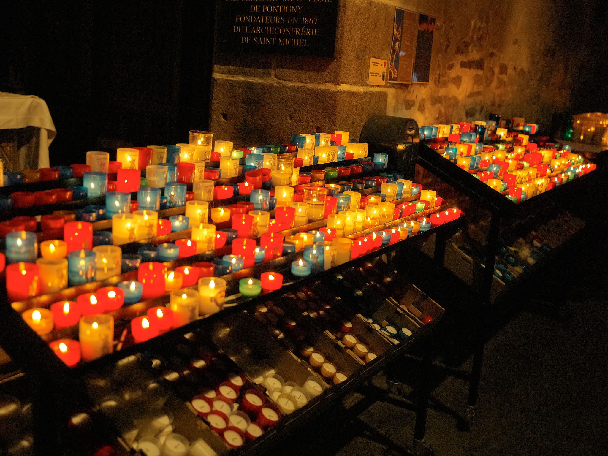 Bougies colorées allumées dans une église sombre.