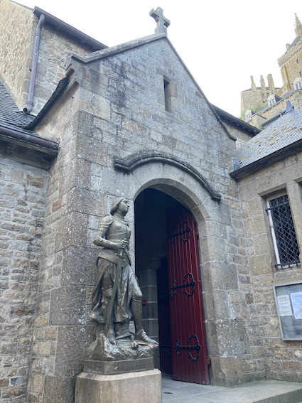 Statue devant une église en pierre, porte rouge.